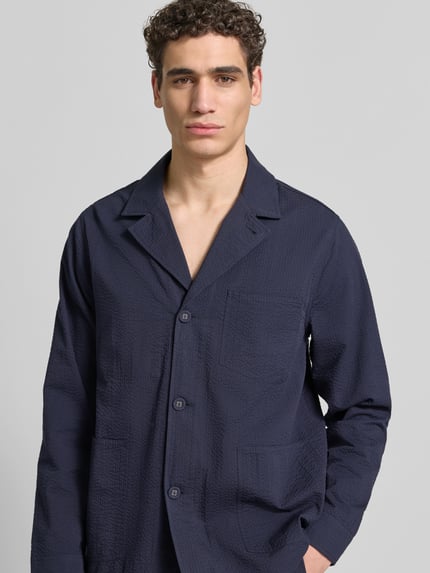 Męski model nosi Relaxed Fit Hemdjacke aus Baumwolle von Officine Générale, kolor granatowy, bawełna, listwa guzikowa, kieszenie, kołnierz z połami, długość tyłu w rozmiarze M: 74 cm, zdjęcie w ujęciu z przodu, półzbliżenie na górną część ciała.