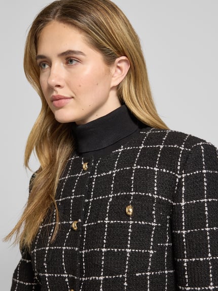 Kobiece modelka nosi Shaped Fit Kurzblazer mit Gitterkaro Modell 'ADINI-1' od HUGO, czarno-biały bouclé, wzór kratka, zapięcie na guziki, zbliżenie górnej części ciała.