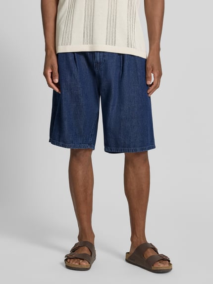 Męski model nosi Regular Fit Jeans-Bermudas aus Baumwoll-Lyocell-Mix Modell 'DENIM' von Armedangels, stylizowana na denim, 5 kieszeni, mieszanka bawełny i lyocellu, naszywka z logo, zapięcie na guzik i zamek, szlufki na pasek, widok całej sylwetki z przodu.