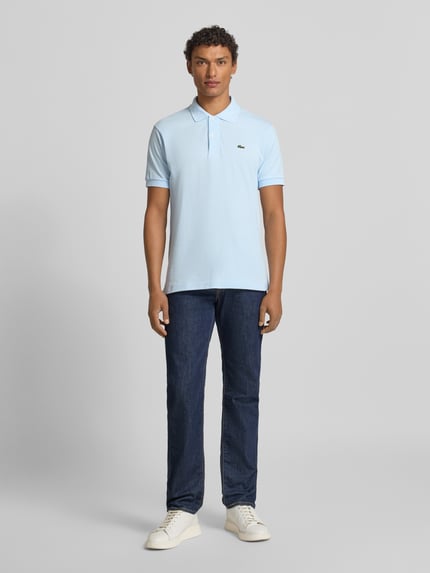 Męskimodel nosi Koszulkę polo z wyhaftowanym logo Model 'L.12.12 CORE' od LACOSTE, bawełna, krój regular fit, jednokolorowy, kołnierzyk polo, listwa guzikowa, prążkowane zakończenia rękawów, długość tyłu 72 cm w rozmiarze M, całkowity widok z przodu.