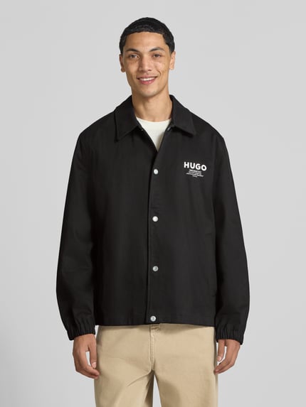 Männermodel trägt Regular Fit Bomberjacke / Blouson aus reiner Baumwolle Modell 'Biyo2631' von HUGO Blue in Schwarz, Ganzkörperansicht von vorne.