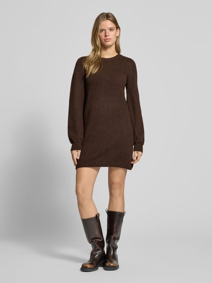 Frauenmodel trägt Strickkleid mit Label-Detail von PIECES in Dunkelbraun, glatte Struktur, kombiniert mit dunklen Stiefeln, Ganzkörperansicht von vorne. Damen Freizeitkleid von PIECES.