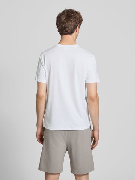 Männermodel trägt weißes T-Shirt mit Logo und Rundhalsausschnitt von CHAMPION, reine Baumwolle, Regular Fit, Rückansicht Ganzkörperansicht.