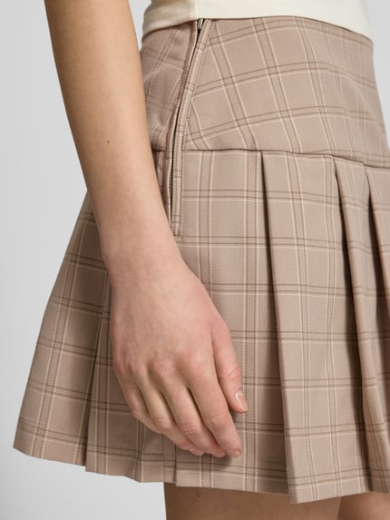 Frauenmodel trägt Faltenrock im Allover-Look von Guess Jeans in Beige mit Karo, Material-Mix mit Viskose-Anteil, Nahaufnahme Oberkörper.