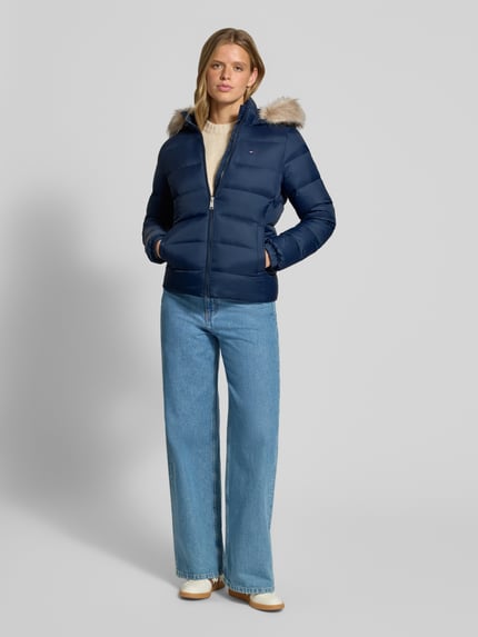 Frauenmodel trägt Regular Fit Daunenjacke mit Kunstfell von Tommy Jeans, dunkelblau, kombiniert mit Jeans, Ganzkörperansicht von vorne. Damen Daunenjacke von Tommy Jeans.