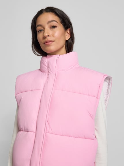 Vrouwenmodel draagt lichtroze Steppweste met Stehkragen Modell 'ROFY' van American Vintage, rechte snit, Nahaufnahme bovenlichaam.