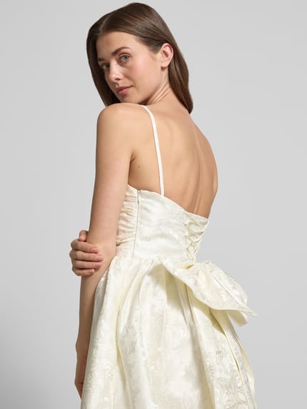 Vrouwenmodel draagt Minikleid met floralem allover-stitching van Hey Kyla, getailleerde en uitlopende pasvorm, sierstrik, afneembare bandjes, ruglengte maat 36: 85 cm, borstwijdte maat 36: 34 cm, lichte crèmekleur met glans, detailopname rugaanzicht.