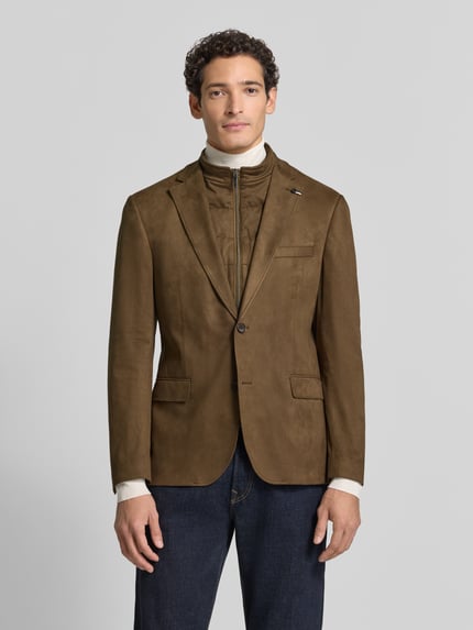 Męski model nosi Regular Fit Sakko aus elastischem Material-Mix mit Label-Detail od bugatti, kolor brązowy, z zamek błyskawiczny, stójka, kołnierz z połami, Brustasza, kieszenie z patką, długość tyłu w rozmiarze 50: 74 cm, szerokość ramion w rozmiarze 50: 43 cm, długość rękawów w rozmiarze 50: 66 cm, Ganzkörperansicht von vorne.