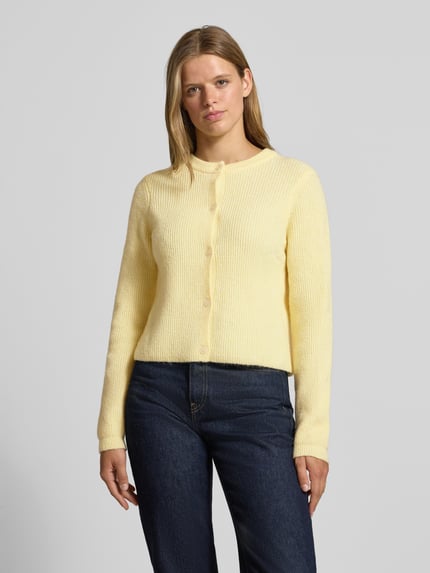 Frauenmodel trägt Strickjacke mit Woll-Anteil Modell 'SILLY' von PIECES in hellgelb mit grober Struktur, kombiniert zu dunkler Jeans, Ganzkörperansicht von vorne.