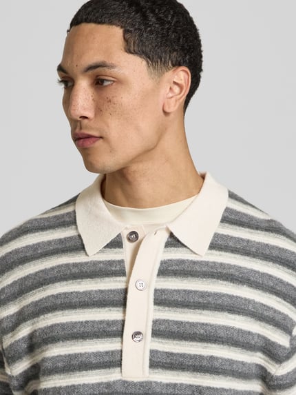 Männermodel trägt Poloshirt mit kurzer Knopfleiste von Officine Générale in grau-beige gestreifter Strickoptik, Nahaufnahme Oberkörper.
