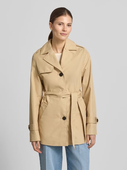 Vrouwenmodel draagt Regular Fit Trenchcoat aus Baumwoll-Mix van s.Oliver RED LABEL in beige, twill, reverskraag, ceintuur, cropped, voorkant, unicolor, waterafstotend, zijzakken, lange mouwen, label-applicatie, knoopsluiting, detail op schouder en rug, geheellichaamsaanzicht van voren.