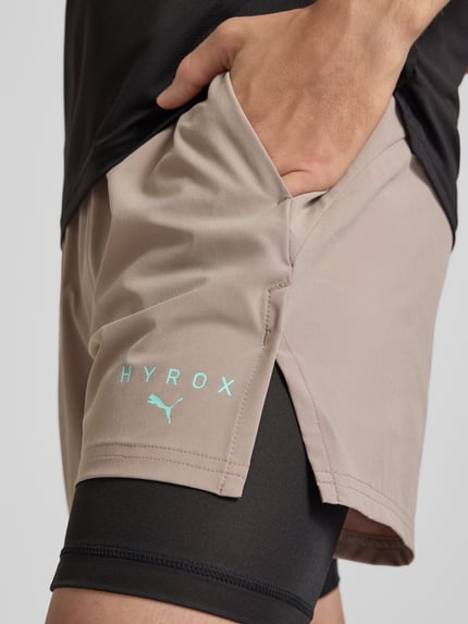 Mężczyznamodel nosi Regular Fit Sportshorts mit Logo-Print model 'PWRMO' od PUMA Performance, beżowy kolor, detal kieszeni, zbliżenie na udo.