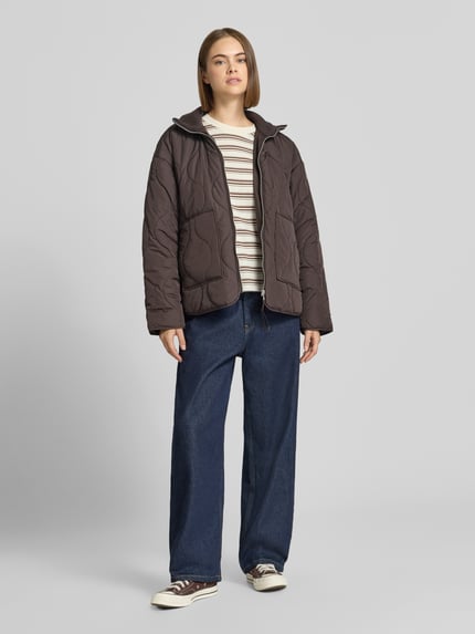 Frauenmodel trägt Steppjacke mit gestricktem Stehkragen Modell 'SERENA' von JJXX in Dunkelbraun, Steppnähte, Ganzkörperansicht von vorne. Damen Steppjacke, Loose Fit, Reißverschluss, seitliche Eingrifftaschen, Rückenlänge 89 cm, Schulterbreite 58 cm, Brustweite 57 cm, Ärmellänge 55 cm.