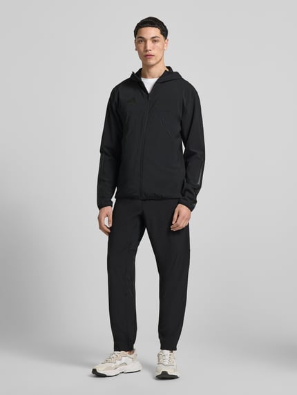 Męskimodel nosi Slim Fit Funktionsjacke aus schnelltrocknendem Material von adidas Sportswear, efekt: jednolity kolor, krój slim fit, kaptur, zamek błyskawiczny, nadruk z logo, długi rękaw, szybkoschnący, z regulacją wilgoci, boczne kieszenie zapinane na zamek błyskawiczny; Ganzkörperansicht von vorne.