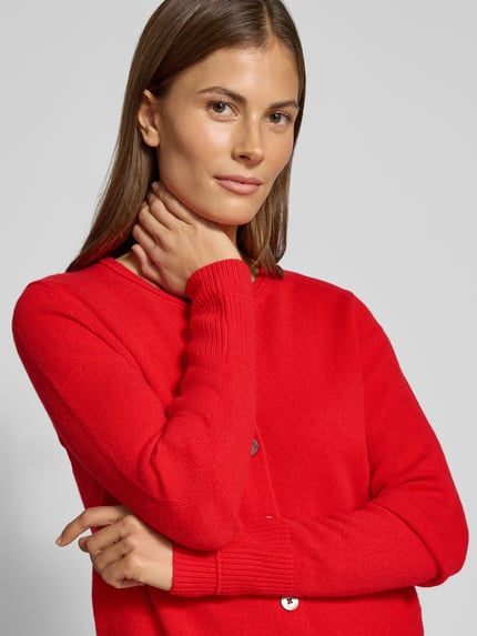 Frauenmodel trägt Cardigan aus Wolle mit Rundhalsausschnitt von Christian Berg Woman in leuchtend Rot, glatte Oberfläche, Nahaufnahme Oberkörper. Reine Wolle, Regular Fit, Knopfleiste, Rückenlänge 58 cm, Ärmellänge 63 cm.