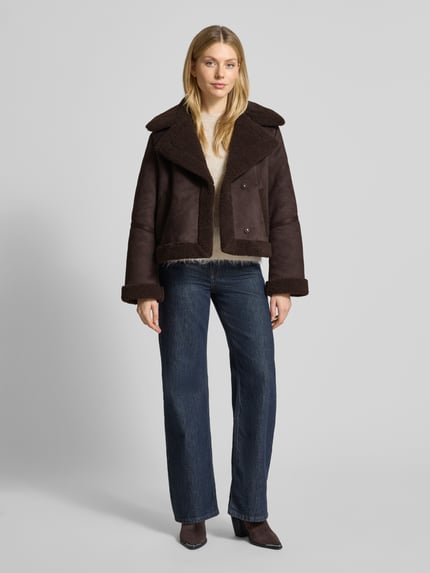 Kobiece modelka nosi Regular Fit Kurtka w imitacji skóry z futerkową podszewką Model 'HARPER' od Vero Moda, efekt: jednolity kolor, wpuszczane kieszenie, kołnierz z połami, zatrzaski, długi rękaw, wykończenie materiału: futerko, widok całej sylwetki z przodu.