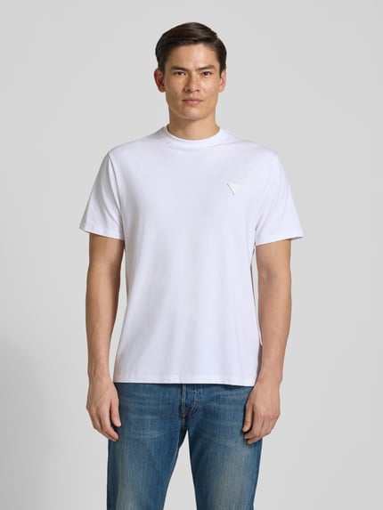 Männermodel trägt T-Shirt mit Logo und Rundhalsausschnitt von Guess, weiß, Baumwoll-Mix mit Modal-Anteil, Relaxed Fit, Ganzkörperansicht von vorne.