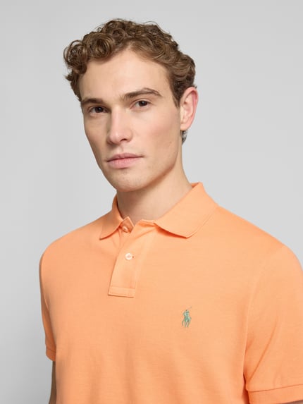 Męski model nosi Slim Fit Koszulkę polo z czystej bawełny Polo Ralph Lauren, efekt: jednolity kolor, pika, detal z logo, kołnierzyk polo, krótki rękaw, wykończenie prążkowane, listwa z guzikami, całkowite zbliżenie na górną część ciała.