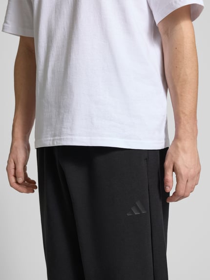 Männermodel trägt Comfort Fit Sweatpants mit Logo-Print von adidas Sportswear, Optik: Unifarben, Materialverarbeitung: Sweat, Nahaufnahme Oberkörper.