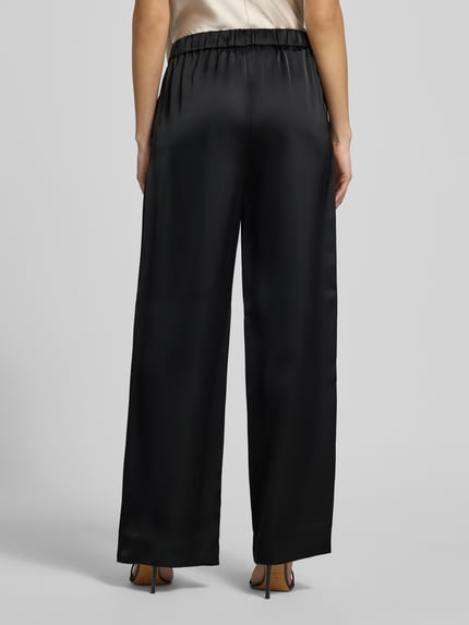 Vrouwenmodel draagt Slim Fit wijdte dames broek met schiebehaken en verdekte ritssluiting model 'HASELI-1' van HUGO, look: effen, high waist, materiaalverwerking: satijn, full body achteraanzicht.