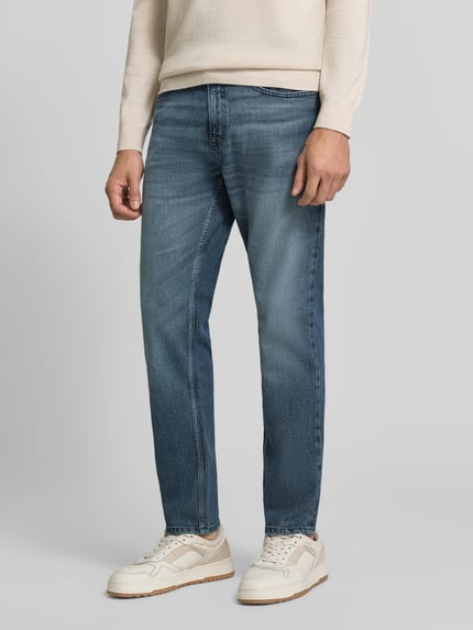 Männermodel trägt Regular Fit Jeans mit Used Waschung Modell 'ONYX SMU' von BOSS Orange, Denim in Medium Wash mit Whiskering, 5-Pocket-Design, Ganzkörperansicht von vorne.
