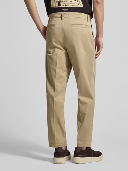 Männermodel trägt Regular Fit Chino aus Baumwoll-Mix Modell 'TAAMIR PLEATED' von Armedangels in Beige mit Gesäßtaschen, Ganzkörperansicht Rückansicht.
