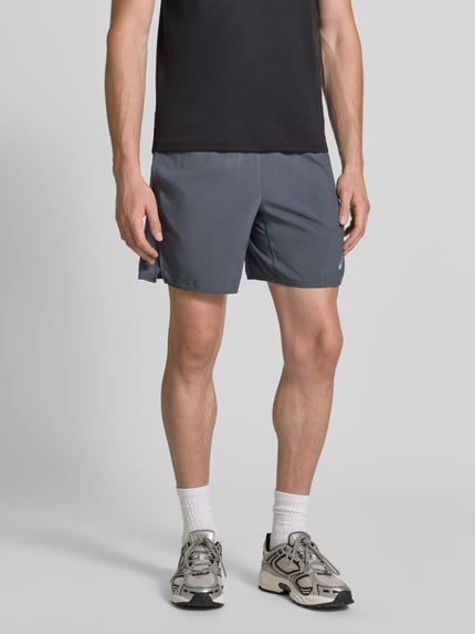 Männermodel trägt Regular Fit Shorts mit integriertem Slip Modell 'Core' von ASICS TIGER in Grau mit Logo-Print, Ganzkörperansicht von vorne. Integrierter Slip, elastischer Bund, Bundweite 38 cm, Innenbeinlänge 17 cm.
