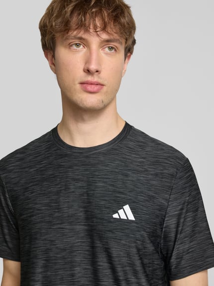 Männermodel trägt T-Shirt mit Label-Print von adidas Training in Schwarz mit Stretch-Anteil und Rundhalsausschnitt, Nahaufnahme Oberkörper.