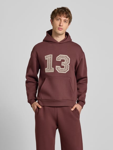 Mannelijk model draagt Hoodie mit Ketten-Stickerei und Känguru-Tasche van REVIEW, katoenmix, regular fit, kangoeroezak, ruglengte maat M 67 cm, mouwlengte maat M 62 cm, bordeauxrood met beige borduursel, Ganzkörperansicht van voren.
