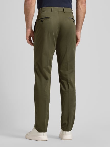 Mężczyzna nosi chinosy Chino mit Eingrifftaschen Modell 'Peaker' von Hiltl, mieszanka bawełny i elastanu, krój regular fit, wpuszczane kieszenie, szerokość w rozmiarze 50: 45 cm, długość wewnętrzna nogawki w rozmiarze 50: 84 cm, zielony kolor, gładka faktura, widok całej sylwetki z tyłu.