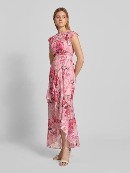 Frauenmodel trägt Regular Fit Abendkleid mit Rüschenbesatz von Lipsy, siateczka, krój regular fit, obszycie falbanami, kwiatowy nadruk na całej powierzchni, z krótkim rękawem, taliowany krój, marszczenia, długość tyłu w rozmiarze 36: 128 cm, szerokość w rozmiarze 36: 40 cm, różowe i czerwone odcienie, lekko połyskująca tekstura, całkowity widok z przodu.