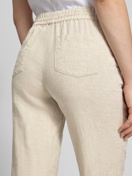 Frauenmodel trägt Leinenhose mit elastischem Bund und Gesäßtaschen von Christian Berg Woman in Beige, Stoffstruktur klar erkennbar, Nahaufnahme Rückansicht. Damen, Reines Leinen, Regular-Fit.