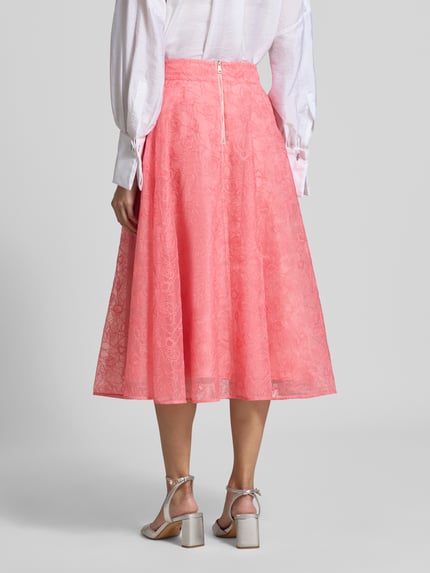 Frauenmodel trägt Midirock mit floralem Allover-Stitching Modell 'Krizie' von Ted Baker in Koralle, A-Linie, Ganzkörperansicht Rückansicht, blickdichter Unterrock, Bundweite 38 cm, Länge 80 cm.