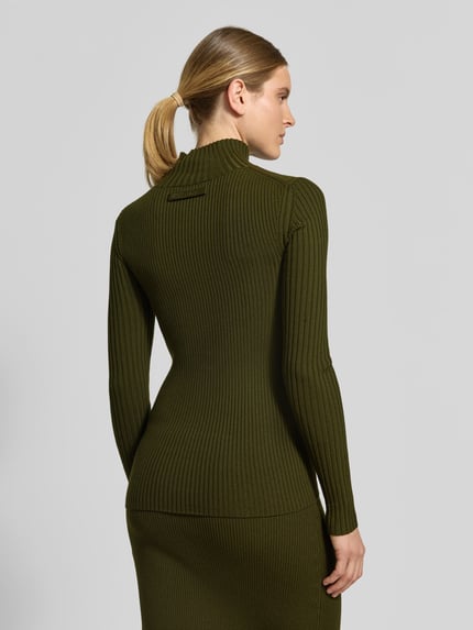 Frauenmodel trägt Longsleeve aus Woll-Mix von Victoria Beckham in Olivgrün, eng anliegend, Strick-Ripp-Optik, Stehkragen, Ganzkörperansicht Rückansicht.