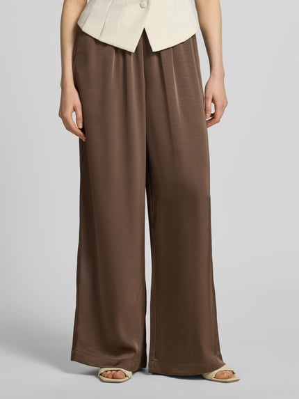 Kobiece modelka ma na sobie spodnie materiałowe Wide Leg Stoffhose aus Baumwoll-Mix Modell 'LUCA' od VILLA SOPHIE, efekt: jednolity kolor, krój: spodnie z szerokimi nogawkami, aplikacja: naszywka z logo, ściągacz: elastyczny, wpuszczane kieszenie; zbliżenie na dolną część ciała, widok z przodu.