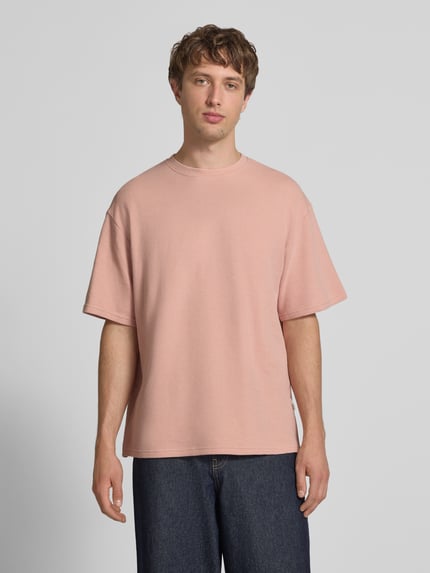 Männermodel trägt Herren T-Shirt mit Strukturmuster und Rundhalsausschnitt Modell 'PETER' von Redefined Rebel aus Baumwoll-Mix in Rosa, Relaxed-Fit, Rückenlänge bei Größe M: 70 cm, Ganzkörperansicht von vorne.