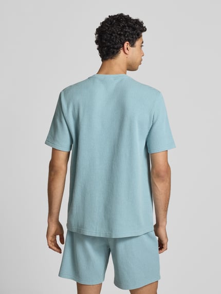 Männermodel trägt T-Shirt mit Strukturmuster und Label-Stitchings von CHAMPION, Baumwoll-Mix, hellblau, Rückansicht Ganzkörperansicht.