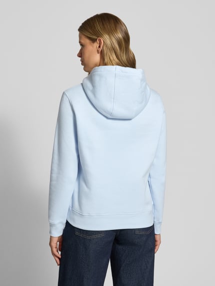 Frauenmodel trägt Regular Fit Hoodie aus Baumwoll-Mix von Tommy Jeans in Hellblau und dunkle Jeans, Ganzkörperansicht Rückansicht. Damen Hoodie von Tommy Jeans.