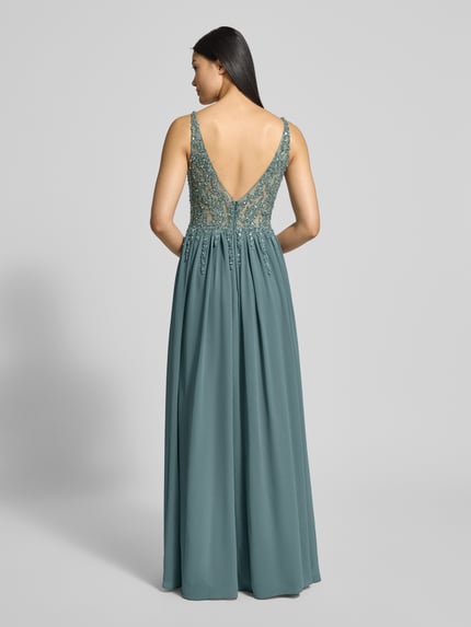 Frauenmodel trägt Abendkleid mit Ziersteinen von Mascara in Blaugrün, taillierte Passform, doppellagiger Rockteil, Ganzkörperansicht Rückansicht. Strapazierfähiges Material, ärmellos, V-Ausschnitt, wattierte Cups, Besatz aus Ziersteinen, Reißverschluss am Rücken, Rückenlänge 150 cm, Brustweite 36 cm.