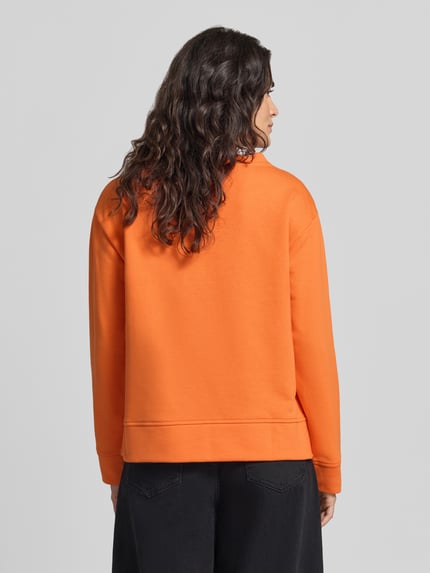Frauenmodel trägt Sweatshirt mit Hundeprint von MILANO ITALY in Orange, langarm, Jersey, gerippte Abschlüsse, Ganzkörperansicht Rückansicht.