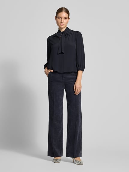 Modelka damska ma na sobie Relaxed Fit Bluse mit Seiden-Anteil von Luisa Cerano, ciemny top z akcentem kokardy, elastyczne mankiety, 3/4 rękaw, acetat z domieszką jedwabiu, widoczna szerokość w rozmiarze 36, długość tyłu 62 cm, długość rękawa 50 cm, całość na tle szarym, widok całej sylwetki z przodu.