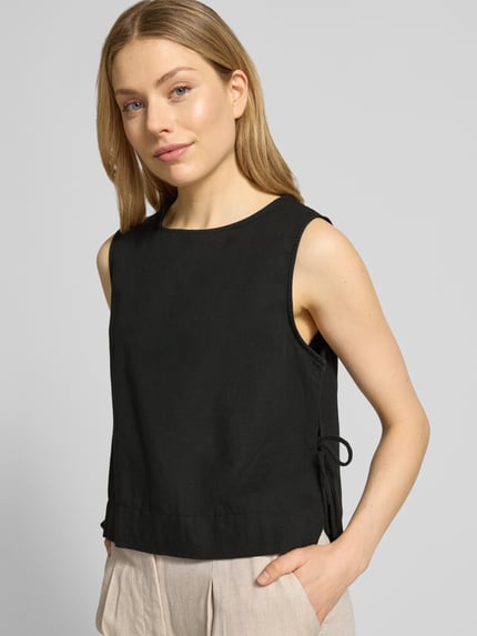 Frauenmodel trägt Blusenshirt mit seitlicher Schnürung Modell 'Svetlana' von Neo Noir, schwarze Reine Baumwolle, lockerer Schnitt, Rundhalsausschnitt, Rückenlänge bei Größe 36 51 cm, Nahaufnahme Oberkörper.
