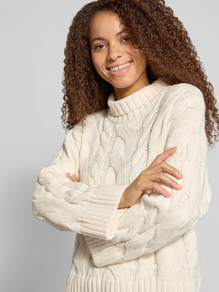 Frauenmodel trägt Regular Fit Strickpullover aus Baumwoll-Mix von Gina Tricot, cremefarbenes Zopfmuster, Stehkragen, Nahaufnahme Oberkörper.