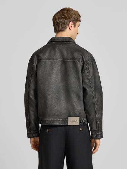 Mężczyzna nosi Regular Fit Kunstlederjacke mit Label-Detail von HUGO, czarna faktura skóry, proste formy, kurtka od HUGO Blue. Ganzkörperansicht Rückansicht.