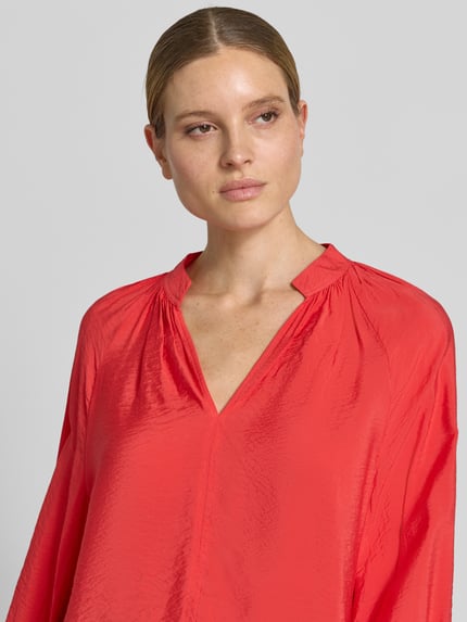 Modelka kobieca nosi Bluse aus Viskose-Mix mit Serafino-Ausschnitt von Christian Berg Woman w kolorze czerwonym, luźny krój, dekolt serafino, sportowe mankiety, długość pleców w rozmiarze 36: 61 cm, długość rękawa w rozmiarze 36: 64 cm, tekstura lekko połyskująca, zbliżenie na górną część ciała