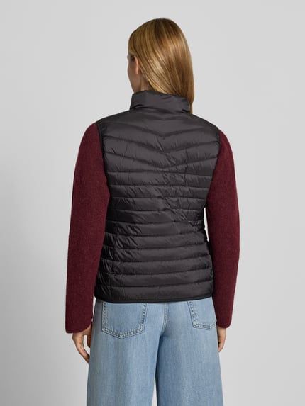 Vrouwenmodel draagt bodywarmer in stiksels van FUCHS SCHMITT, getailleerde pasvorm, opstaande kraag, tweewegritssluiting, ruglengte maat 36: 55 cm, schouderbreedte maat 36: 39 cm, borstwijdte maat 36: 48 cm, zwart met bordeaux, doorgestikte structuur, volledige achteraanzicht.