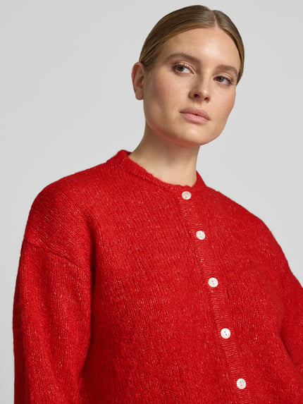 Frauenmodel trägt Relaxed Fit Strickjacke mit Woll-Anteil Modell 'Belablue' von ICHI in kräftigem Rot, weiße Knopfleiste, Nahaufnahme Oberkörper. Damen Strickjacke, elastischer Material-Mix, Rundhalsausschnitt, gerippte Bündchen.