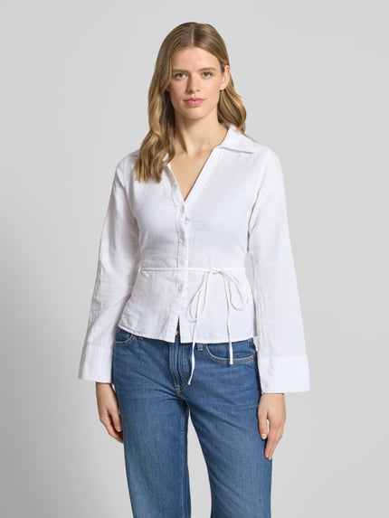 Frauenmodel trägt Leinenbluse mit Bindegürtel und V-Ausschnitt von Gina Tricot in Weiß, taillierter Schnitt, Baumwoll-Leinen-Mix, Kentkragen, Knopfleiste, Rückenlänge 60 cm, Ärmellänge 64 cm, Ganzkörperansicht von vorne.
