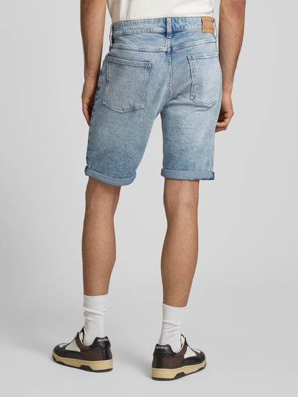 Männermodel trägt Regular Fit Jeansshorts aus Baumwoll-Mix Modell 'RONNIE' von Tommy Jeans in hellblauem Denim mit Label Patch, Ganzkörperansicht Rückansicht.