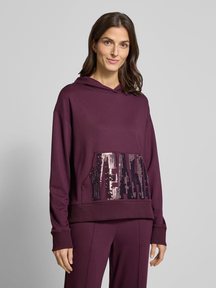 Frauenmodel trägt Hoodie aus Viskose-Mix mit Känguru-Tasche und Pailletten von Milano Italy, Relaxed-Fit, Ganzkörperansicht von vorne.